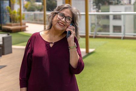 Attractive smiling senior woman talking on cell phone in a garden on a summer morningの写真素材
