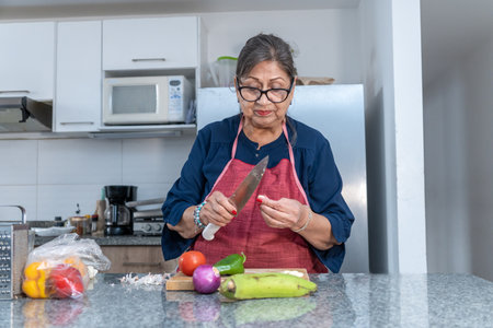 A woman is cutting vegetables on a counter. She is wearing a red apron and has a knife in her handの写真素材