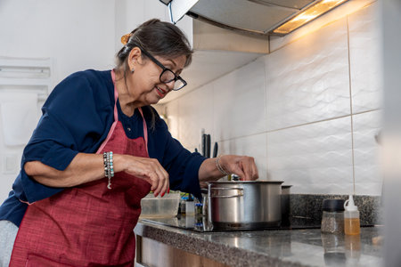 Happy retired woman adding spices to pot on stoveの写真素材