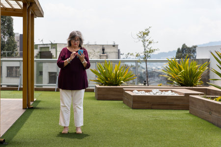 Elderly woman using smartphone in a rooftop garden, enjoying the convenience of modern technologyの写真素材