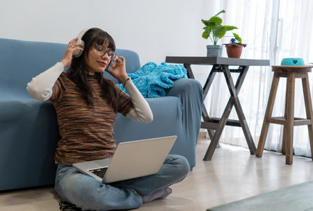 Girl enjoying music with headphones and working on laptop sitting on the floor in her living roomの写真素材