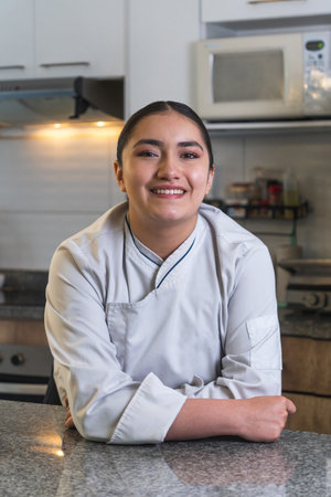 Portrait of a young smiling latin woman chef with arms crossed, posing in a professional kitchenの写真素材