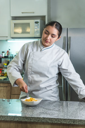 Female chef arranging pasta in a bowl in a modern kitchenの写真素材