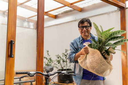 Happy man bringing potted plant wrapped in burlap home, enjoying gardening hobbyの写真素材