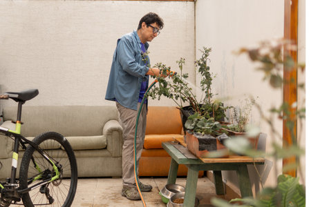 Man watering strawberries and herbs on a patio, fostering a sustainable urban gardenの写真素材