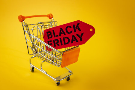 Miniature shopping cart carrying a red black friday tag on a vibrant yellow background, symbolizing upcoming sales and consumerismの写真素材