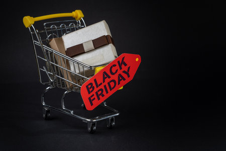 Miniature shopping cart carrying wrapped gifts and a black friday tag, symbolizing the shopping frenzy during salesの写真素材