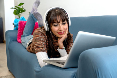 Woman enjoying video content or music at home on sofa with headphones and laptopの写真素材