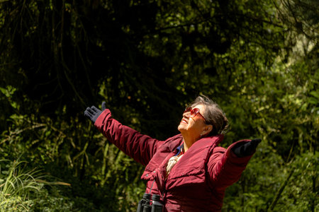 Senior woman standing outdoors with outstretched arms, celebrating joy and sunlight in a forestの写真素材