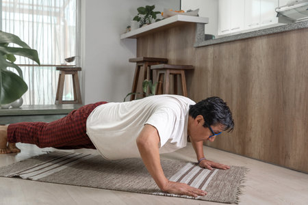 Mature man exercising, holding a plank position on a rug in his living room