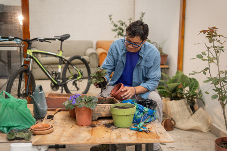 Person repotting a plant from a plastic pot to larger container, enjoying gardening at homeの写真素材