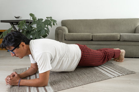 Man doing a plank exercise indoors on a rug, strengthening his core musclesの写真素材
