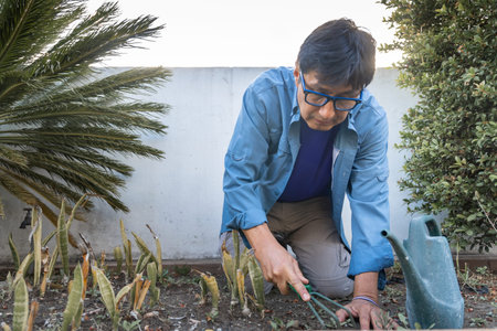 Man kneeling while weeding a garden bed using a hand cultivator