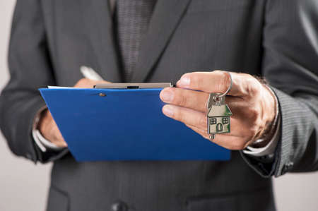 Estate agent giving house keys on a silver house shaped keychainの写真素材
