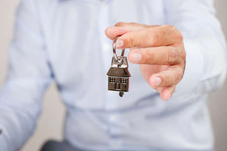 Estate agent giving house keys on a silver house shaped keychainの写真素材