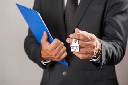 Estate agent giving house keys on a silver house shaped keychainの写真素材
