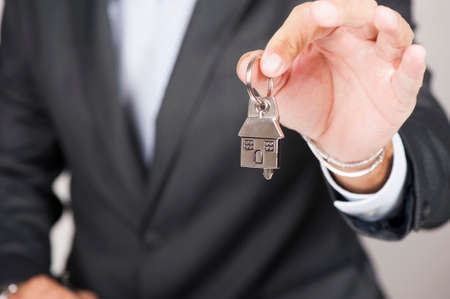 Estate agent giving house keys on a silver house shaped keychainの写真素材