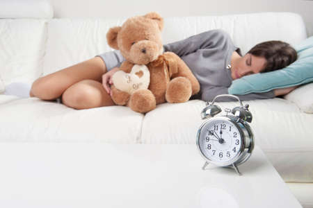 Alarm clock on table and woman laying on sofa