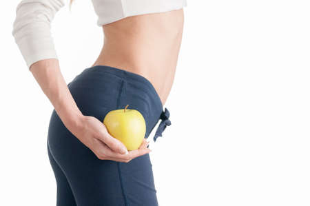 Young slim woman holding an apple and wearing oversize jeans on white