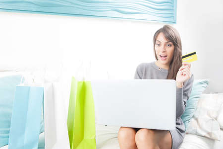 Online shopping concept. Smiling woman sitting on sofa with laptopの写真素材