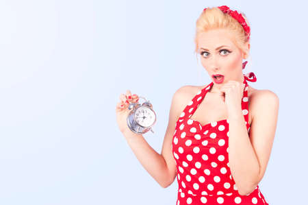 Blonde girl in a red vintage dress looking surprised on vintage alarm clockの写真素材