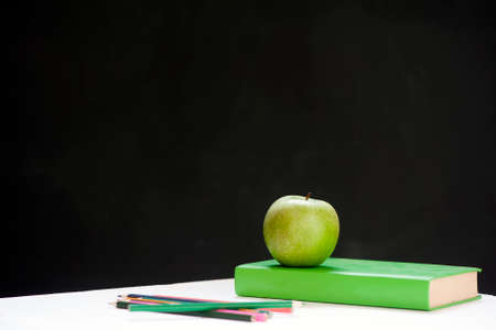 Green apple on green book against blackboard