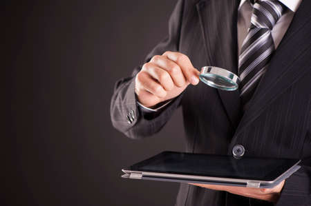 Businessman holding magnifying glass and digital tablet. Searching and examining conceptの写真素材