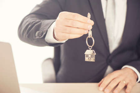 Estate agent giving house keys on a silver house shaped keychainの写真素材