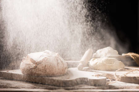 Freshly baked bread on wooden table on dark background with flour on the air