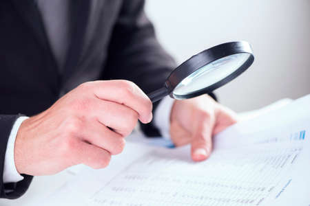 Businessman checking a tablet with magnifying glass の写真素材