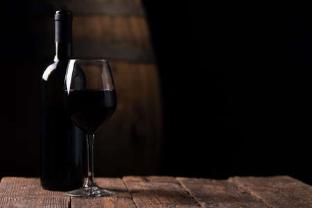 A bottle opf red wine and a glass with barrel on background