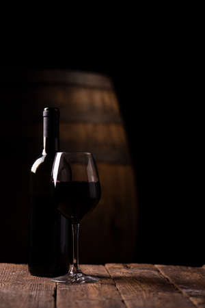 A bottle opf red wine and a glass with barrel on backgroundの写真素材