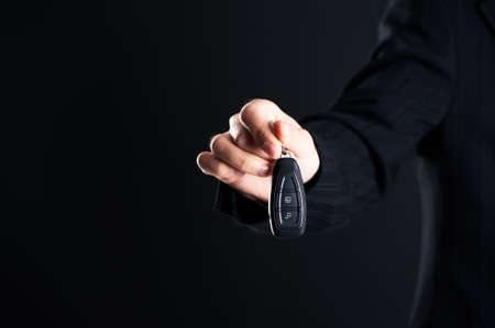 Car salesman handing over your new car keys, dealership and sales concept on a dark backgroundの写真素材