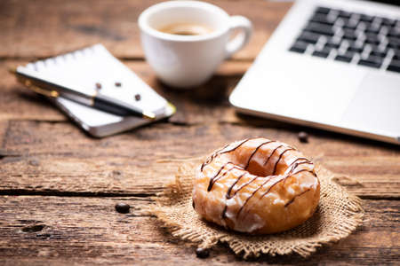 Coffee break. Doughnut on desk with a notebook pad and coffeeの写真素材