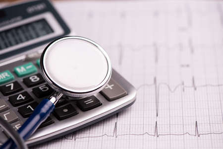 EKG with  stethoscope and calculator showing cost of health care. Close up