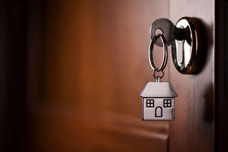 House key on a house shaped silver keyring in the lock of a door