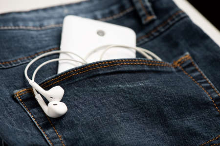 Smartphone in the front pocket of blue jeans and white headphone. Close upの写真素材