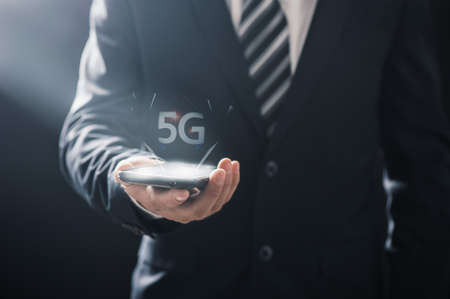 Business man using mobile smartphone with 5G icons flow on virtual screen concept. 5G High speed internet networkの写真素材