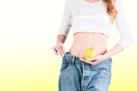 Young woman in jeans weight loss slimming with appleの写真素材