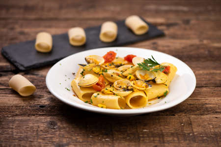 Paccheri pasta with clams on white plate on rustic wooden tableの写真素材