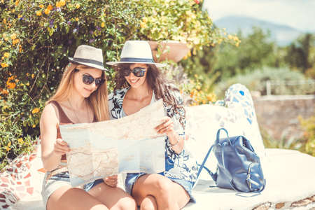 Two young smiling tourist women are sitting looking a map for the direction on a sunny dayの写真素材
