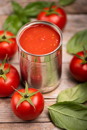 Open tin of tomatoes sauce with whole fresh tomatoes on a rustic wooden table. Close upの写真素材