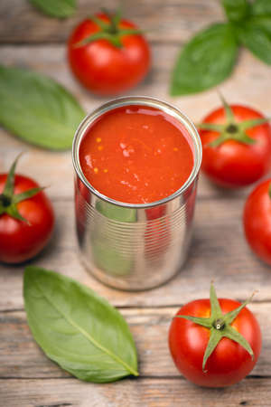 Open tin of tomatoes sauce with whole fresh tomatoes on a rustic wooden table. Close up