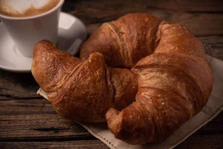 Fresh buttery croissants with coffee on rustic wooden table close up