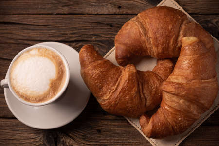 Fresh buttery croissants with coffee on rustic wooden table close up