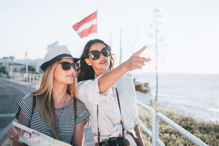 Two beautiful blonde and brunette women with tourist map on holiday. Holidays and tourism conceptの写真素材
