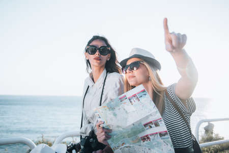 Two beautiful blonde and brunette women with tourist map on holiday. Holidays and tourism conceptの写真素材