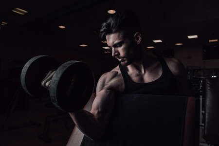 Muscular man working out in gym doing exercises with dumbbells at biceps Close upの写真素材