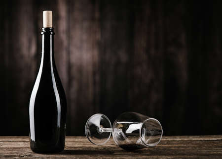 Red wine bottle with empty wine glass on dark wooden table close upの写真素材