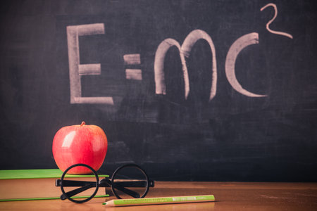 Equation E = mc2 handwritten on blackboard with apple and bookの写真素材
